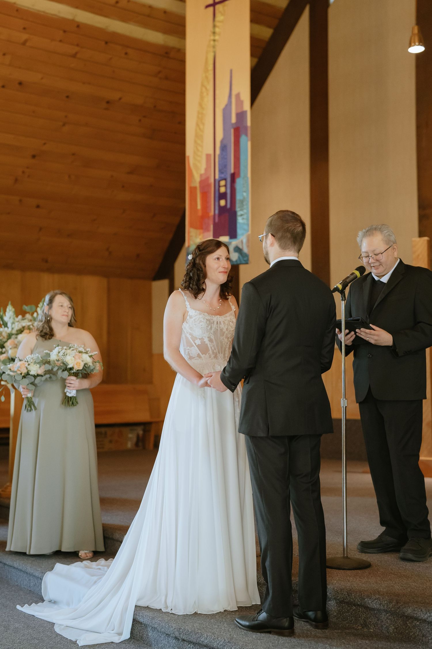 Melissa in a lace wedding gown holding hands with Michael at the altar while the officiant speaks.