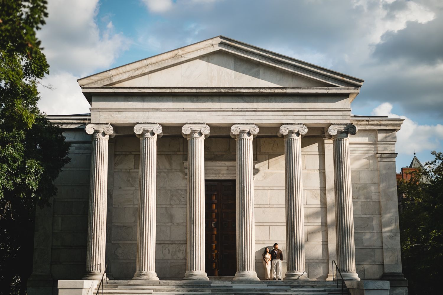 Couple standing together on steps of a grand neoclassical building with tall white columns.