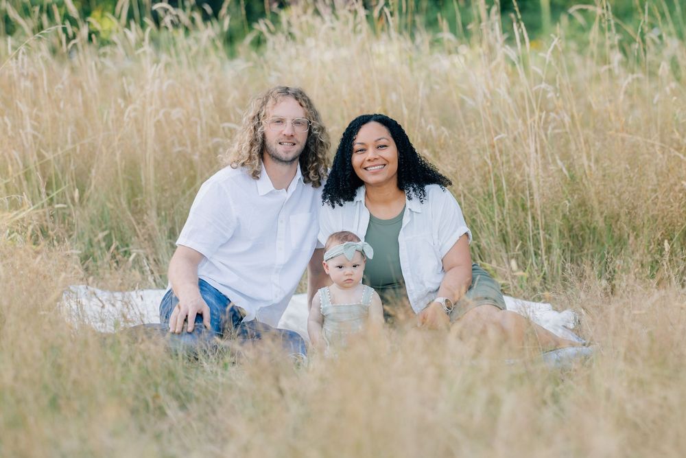 Happy interracial family with baby sitting in golden field grass for outdoor portrait session.