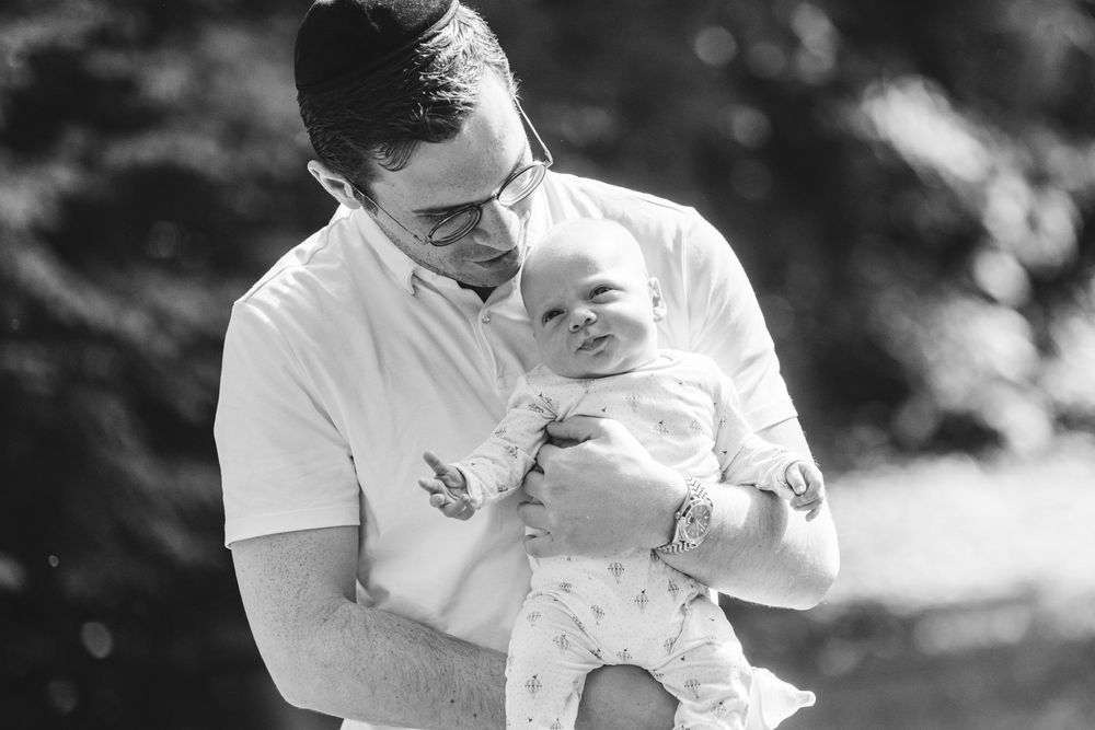 Black and white photo of a father holding his newborn baby outdoors, sharing a tender moment.