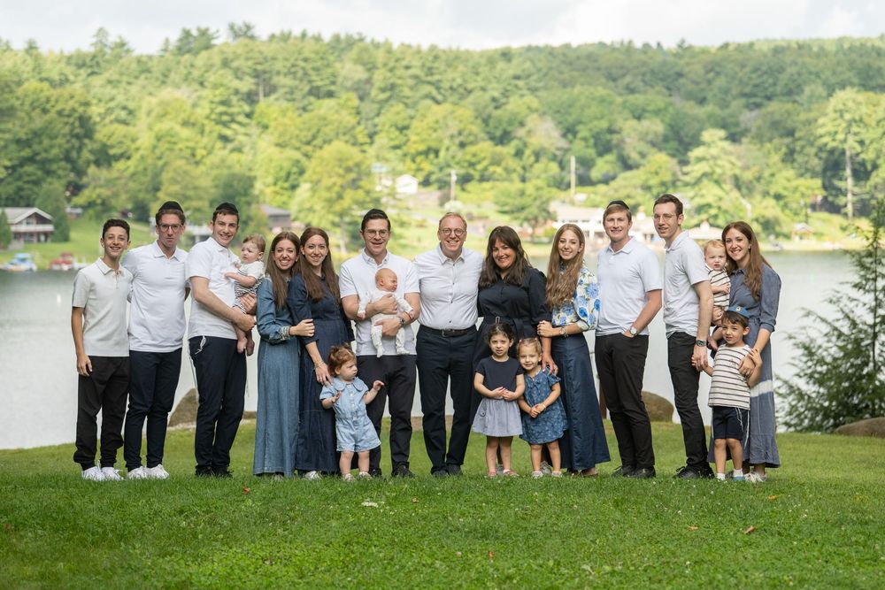 Large family group portrait outdoors near a lake, including adults and young children smiling together.