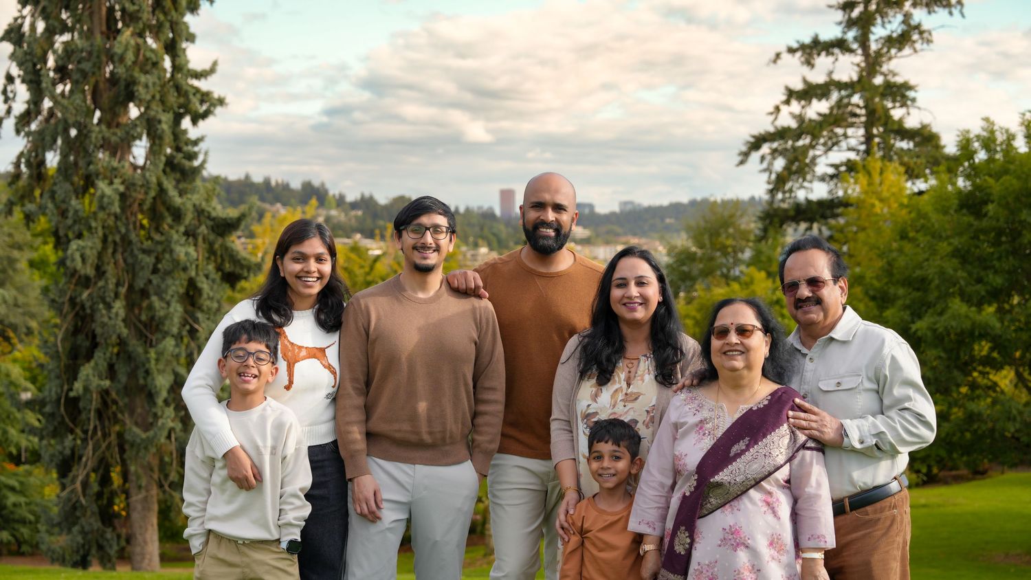 Indian family of seven smiling together outdoors in a lush green park setting during golden hour.