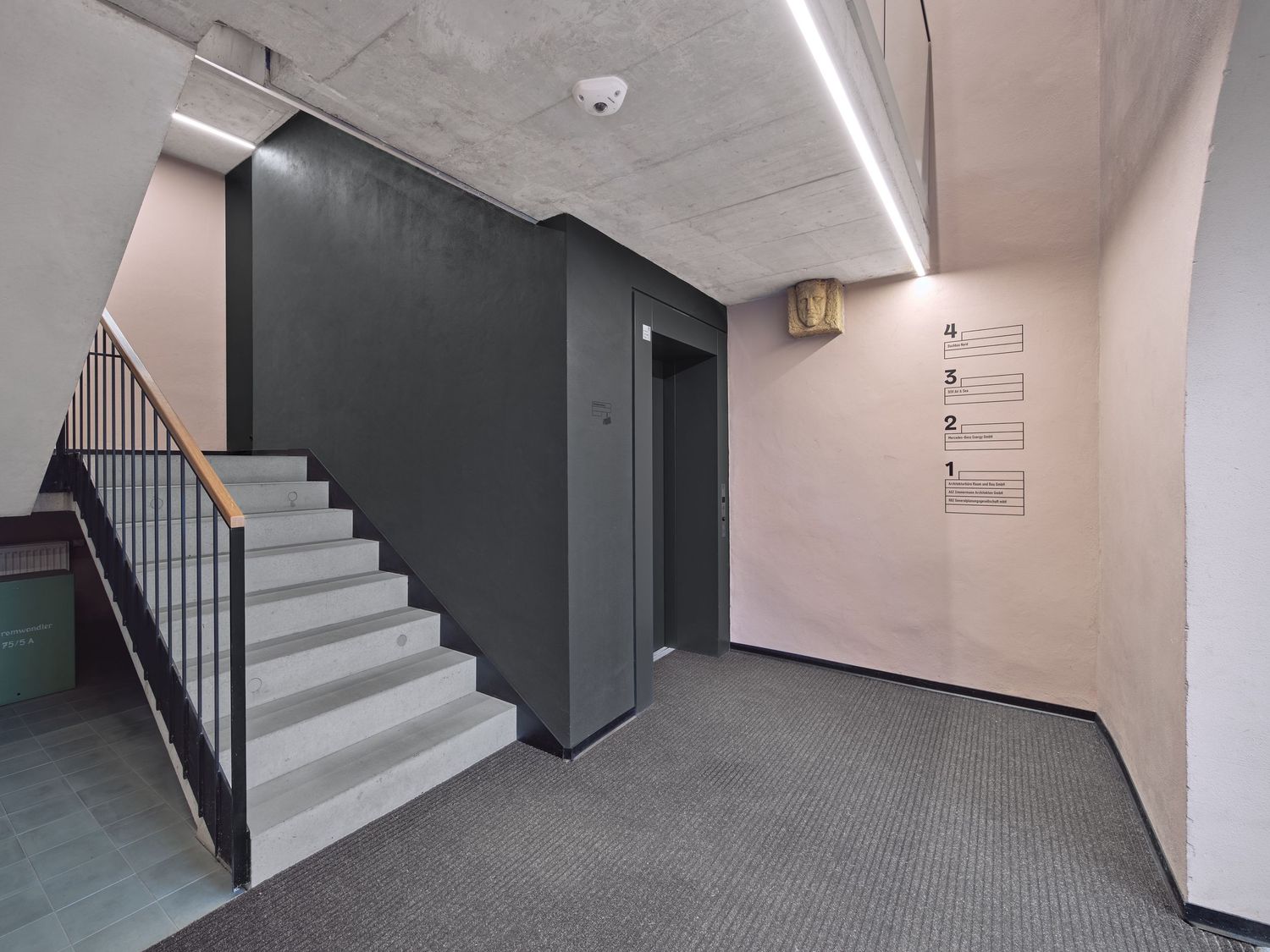Modern building stairwell with concrete steps, metal railing, dark gray elevator doors and a floor directory sign on a pink wall.