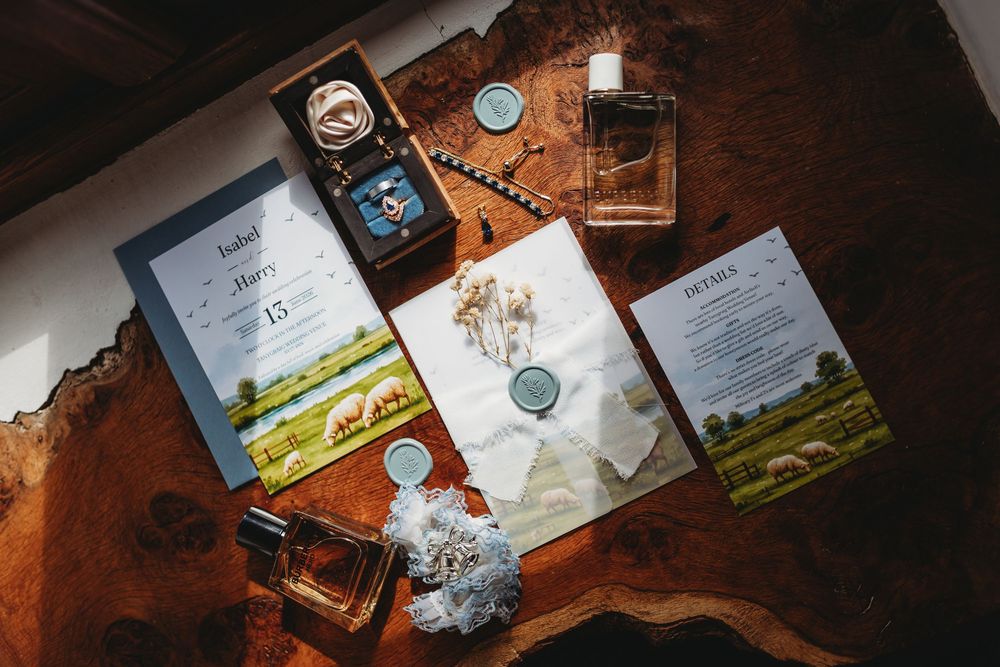 Elegant wedding flat lay with floral invitations, wax seals, perfume bottles, and accessories on a rustic wooden table.