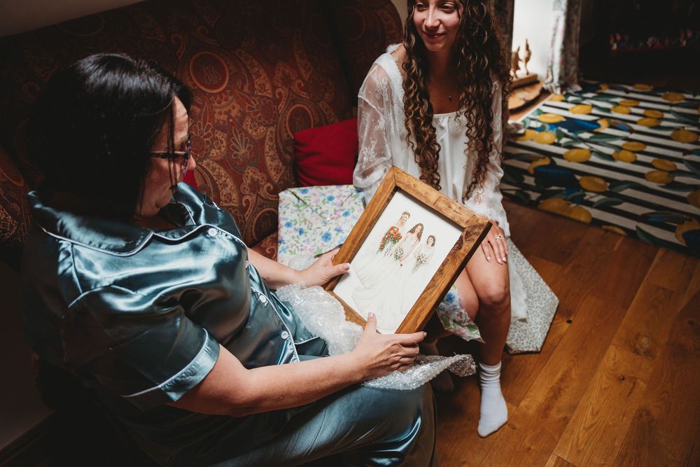 Two women smiling while examining a framed portrait together in a cozy decorated room.