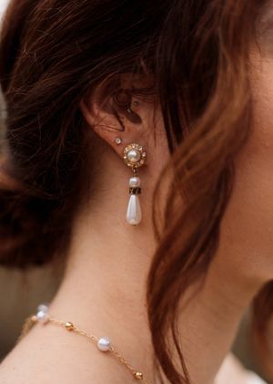 Close-up of a bride's ear adorned with a gold and pearl teardrop earring and a matching pearl necklace.