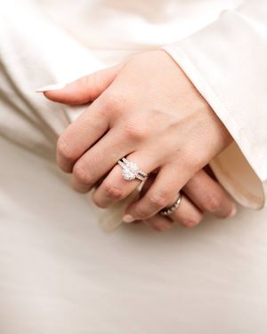 Close-up of a bride's hands resting on a white satin dress, showing a sparkling diamond engagement ring and wedding band set.