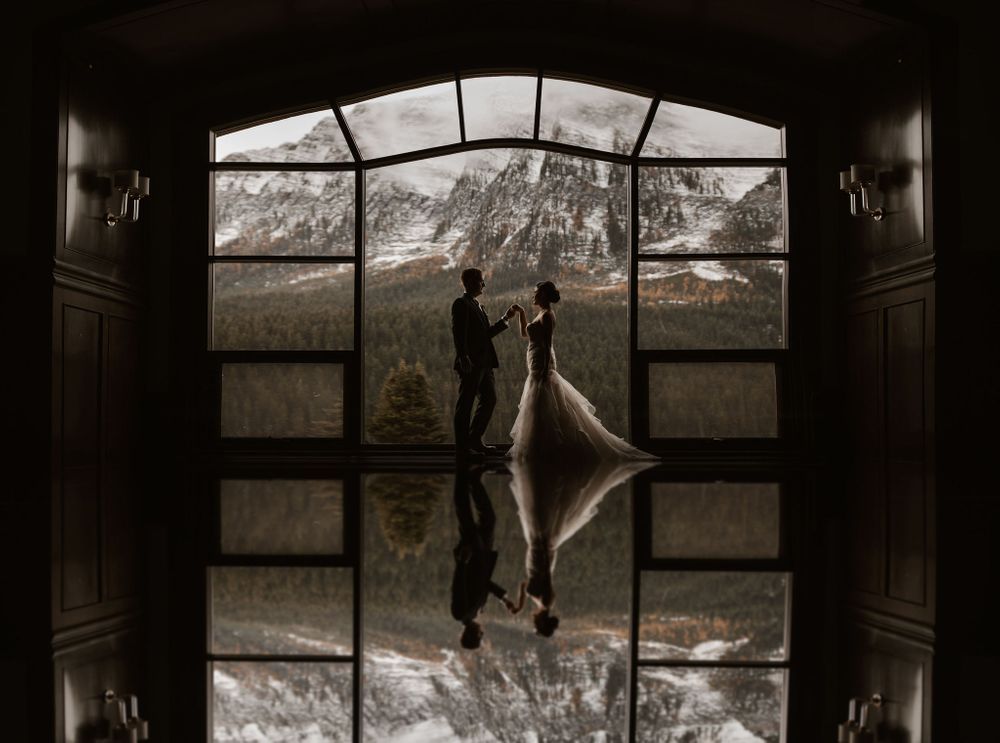 Bride and groom embrace with snowy mountain peaks behind them in a romantic winter wedding portrait.