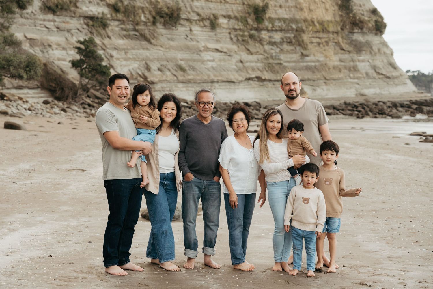 Family of six walking barefoot on a beach, smiling and holding hands, dressed in white and black casual outfits.