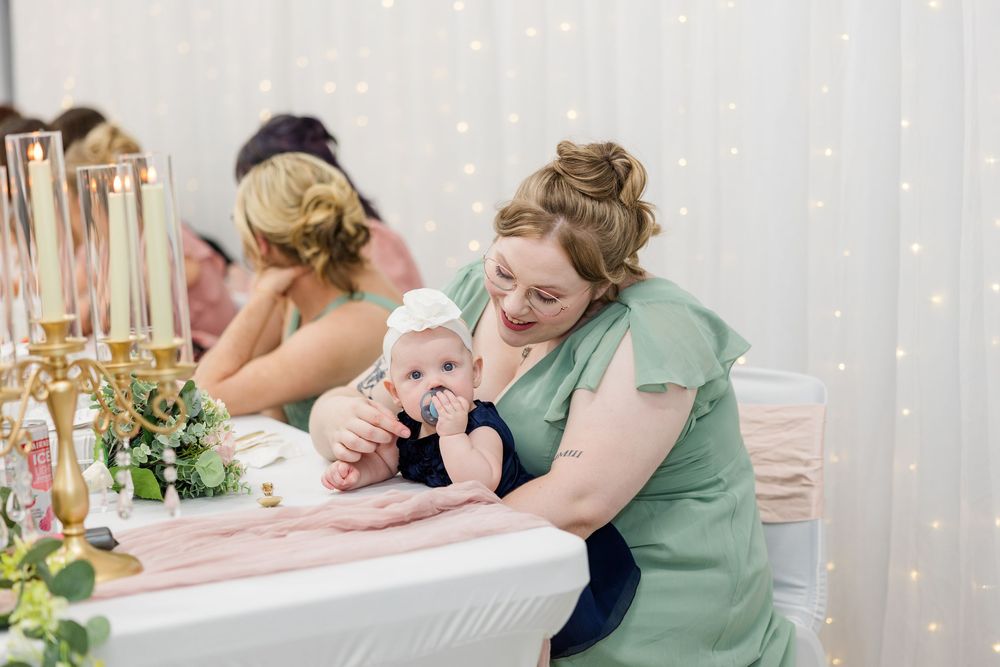 Woman in green dress holding a baby at an elegant wedding reception with gold candelabras and fairy lights.