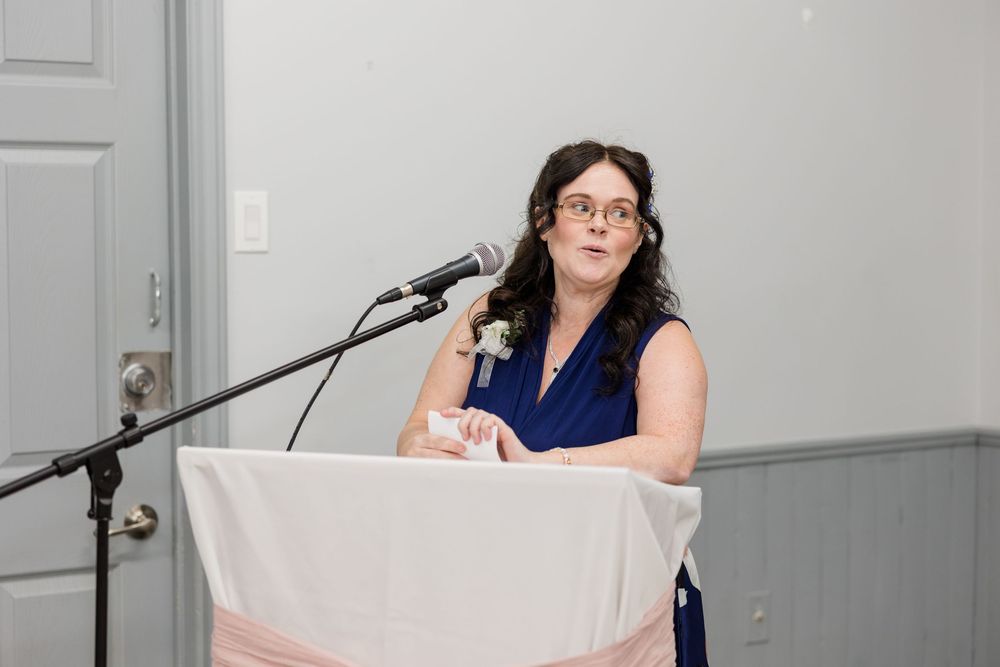 Woman in blue dress speaking at podium with microphone at indoor event.