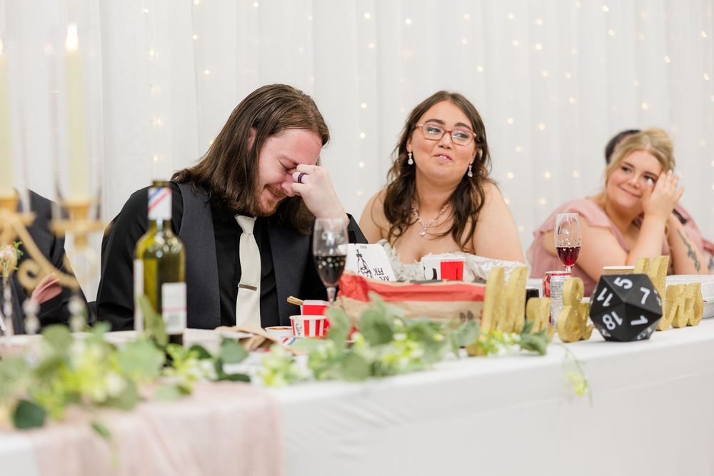 Emotional wedding guests crying and laughing at head table during heartfelt reception speech at elegant venue.