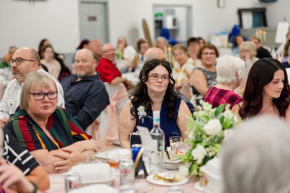 Guests seated at round tables during wedding reception in decorated hall with floral centerpieces.
