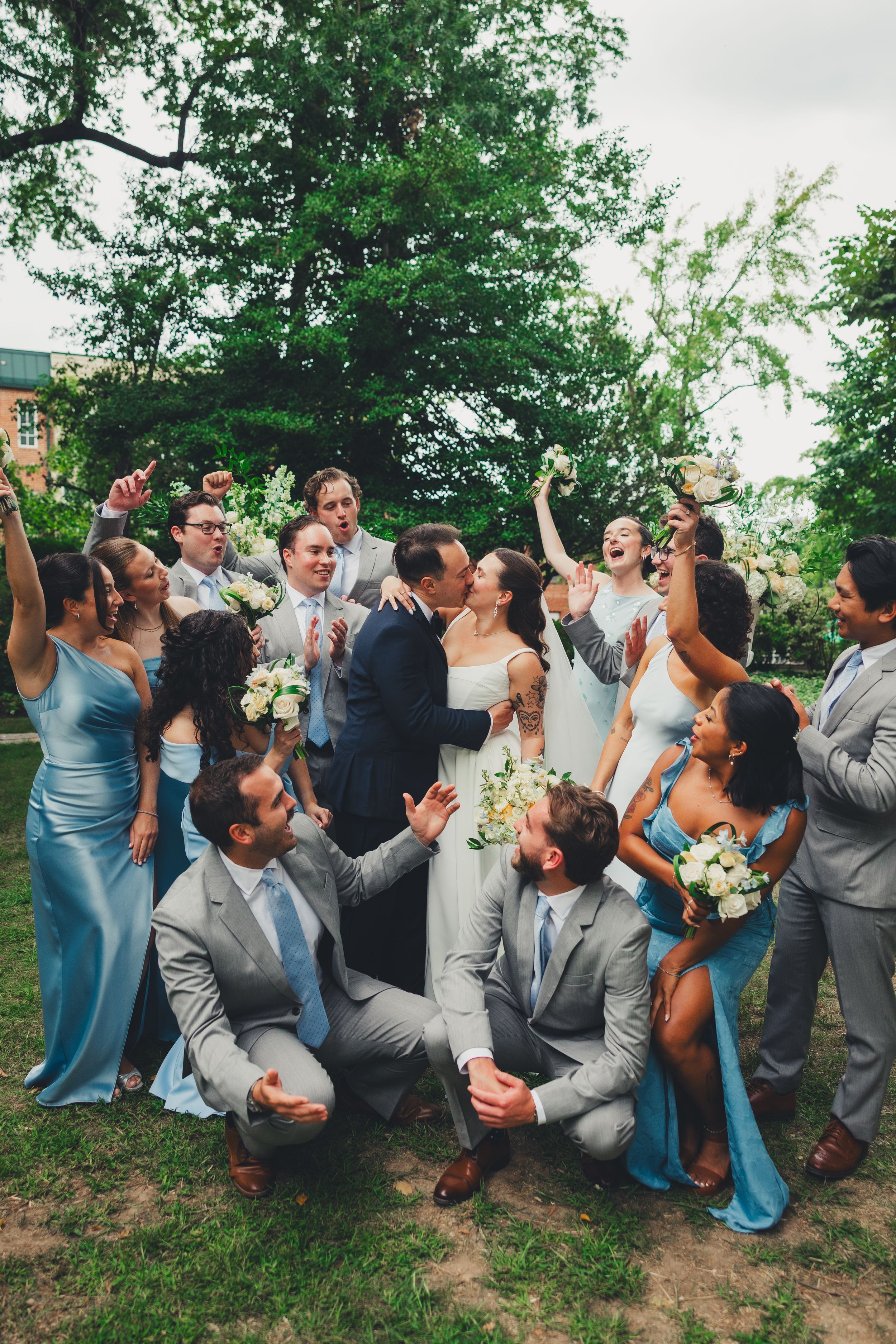 Washington DC Wedding party celebrates as bride and groom share a kiss outdoors, bridesmaids in blue gowns and groomsmen in gray suits