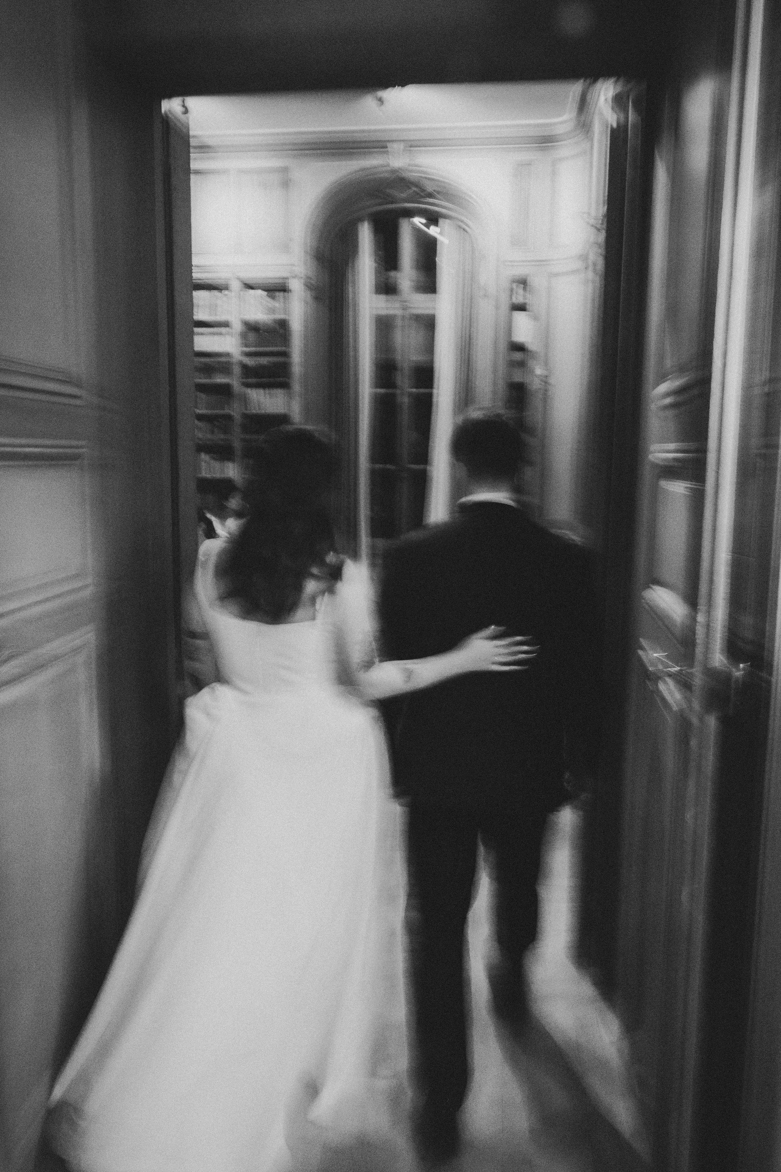 Black and white photo of bride and groom walking hand in hand through an elegant doorway at their wedding.