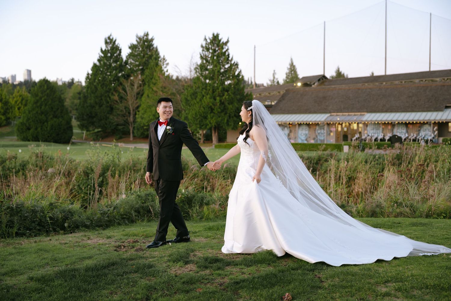 A bride and groom walk hand in hand across a lush green lawn during their outdoor wedding ceremony.