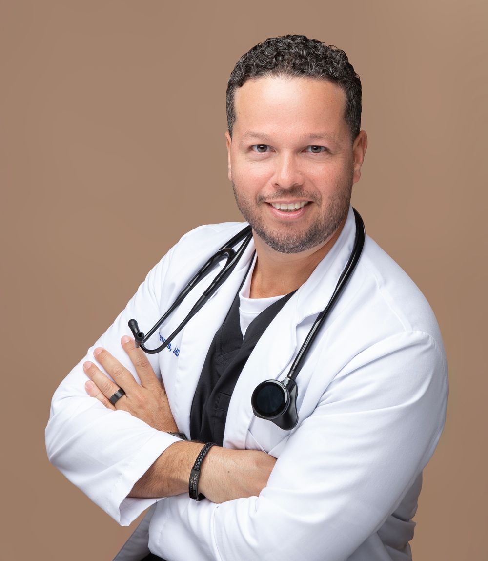 Physician in a white coat with arms crossed on a tan backdrop, professional headshot for men