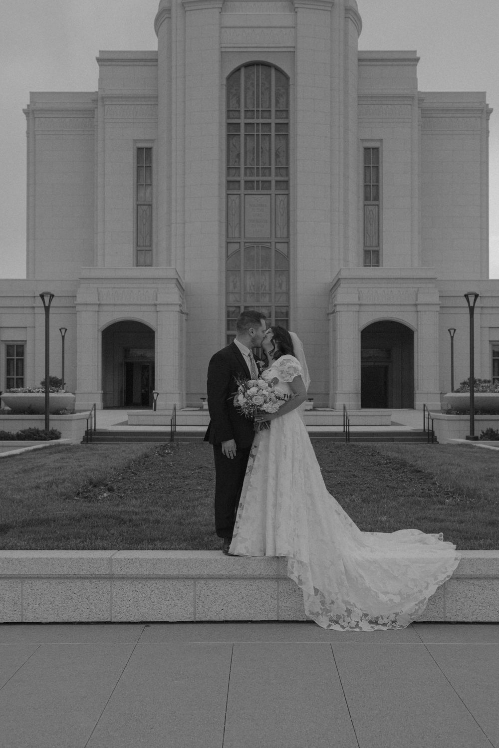 Black and white photo of a bride and groom kissing in front of an LDS temple on their wedding day.