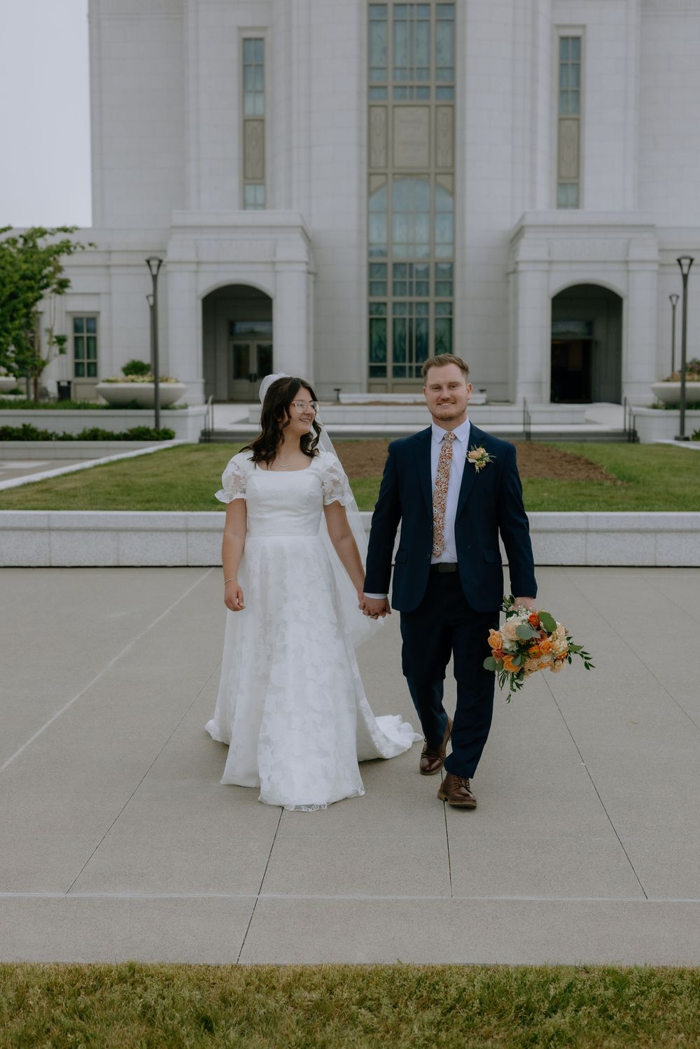 Bride and groom walking hand in hand outside a white temple on their wedding day.
