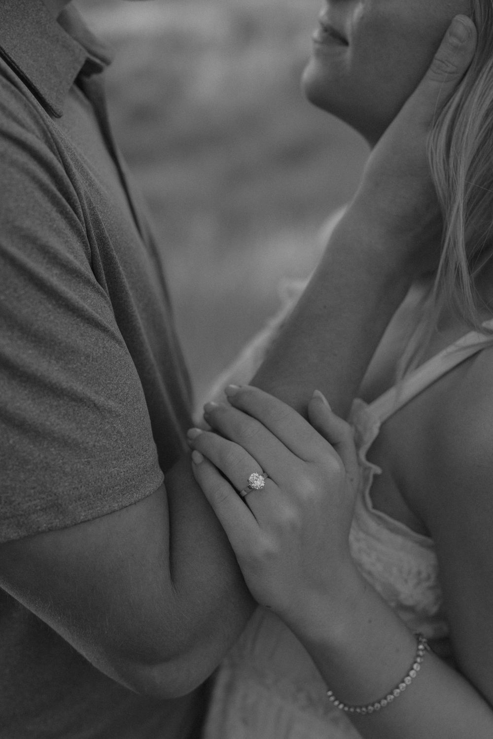 Close-up of a couple holding hands showing an engagement ring in black and white.