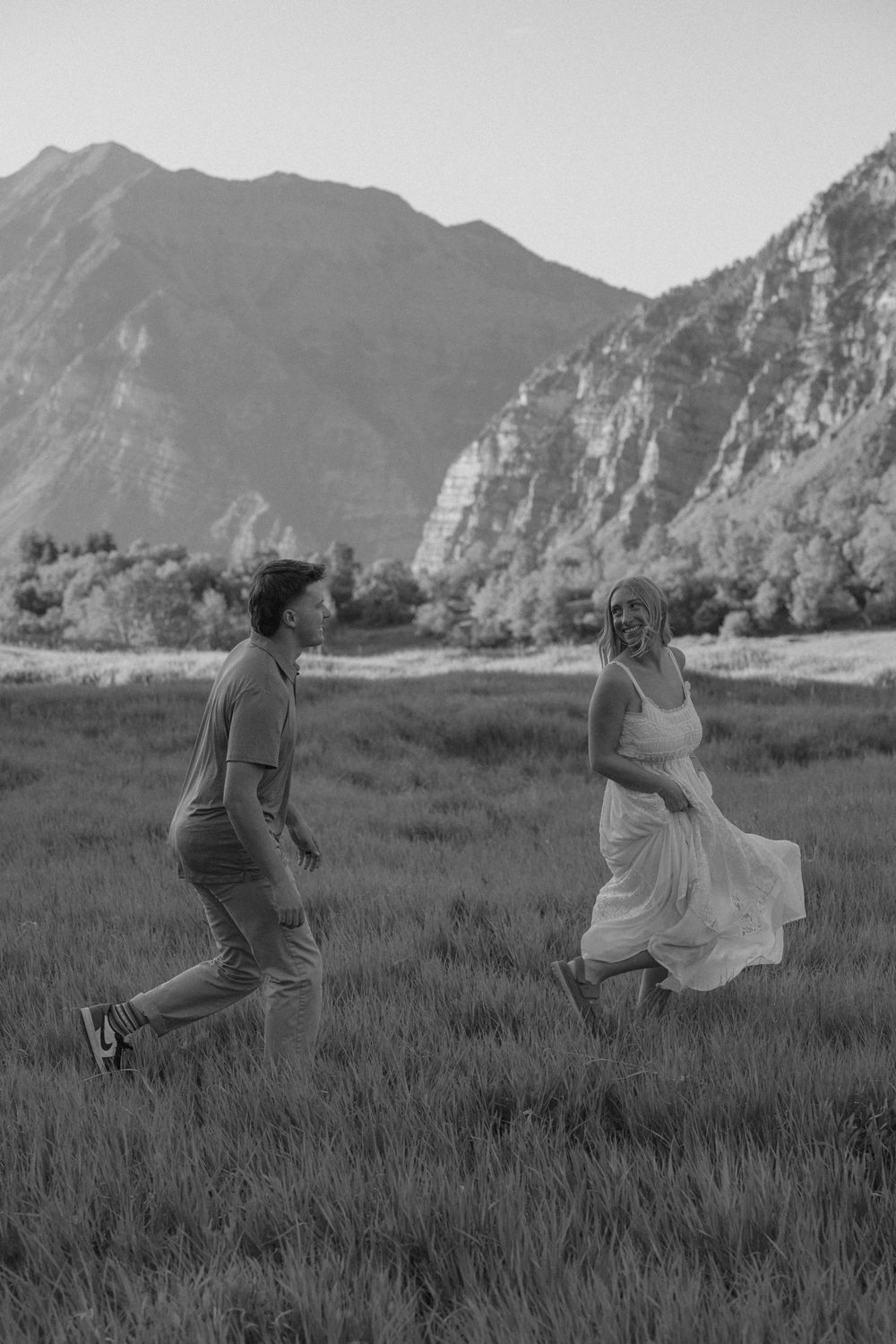 Couple running and laughing in a grassy mountain field, black and white photo.