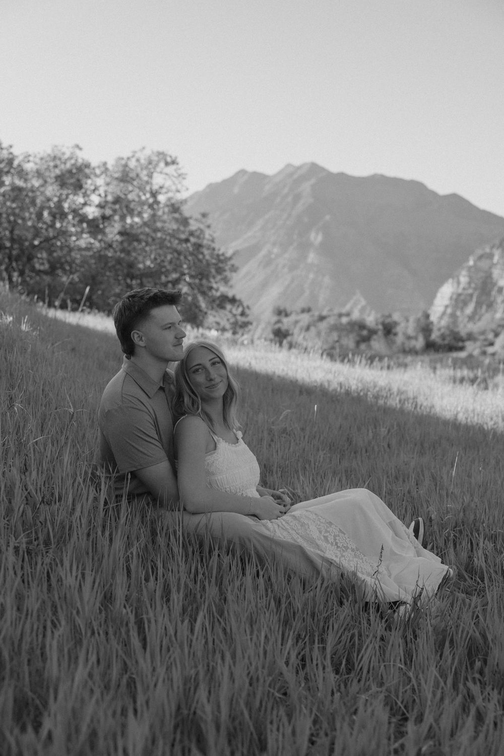 Black and white photo of couple sitting in mountain grass field.