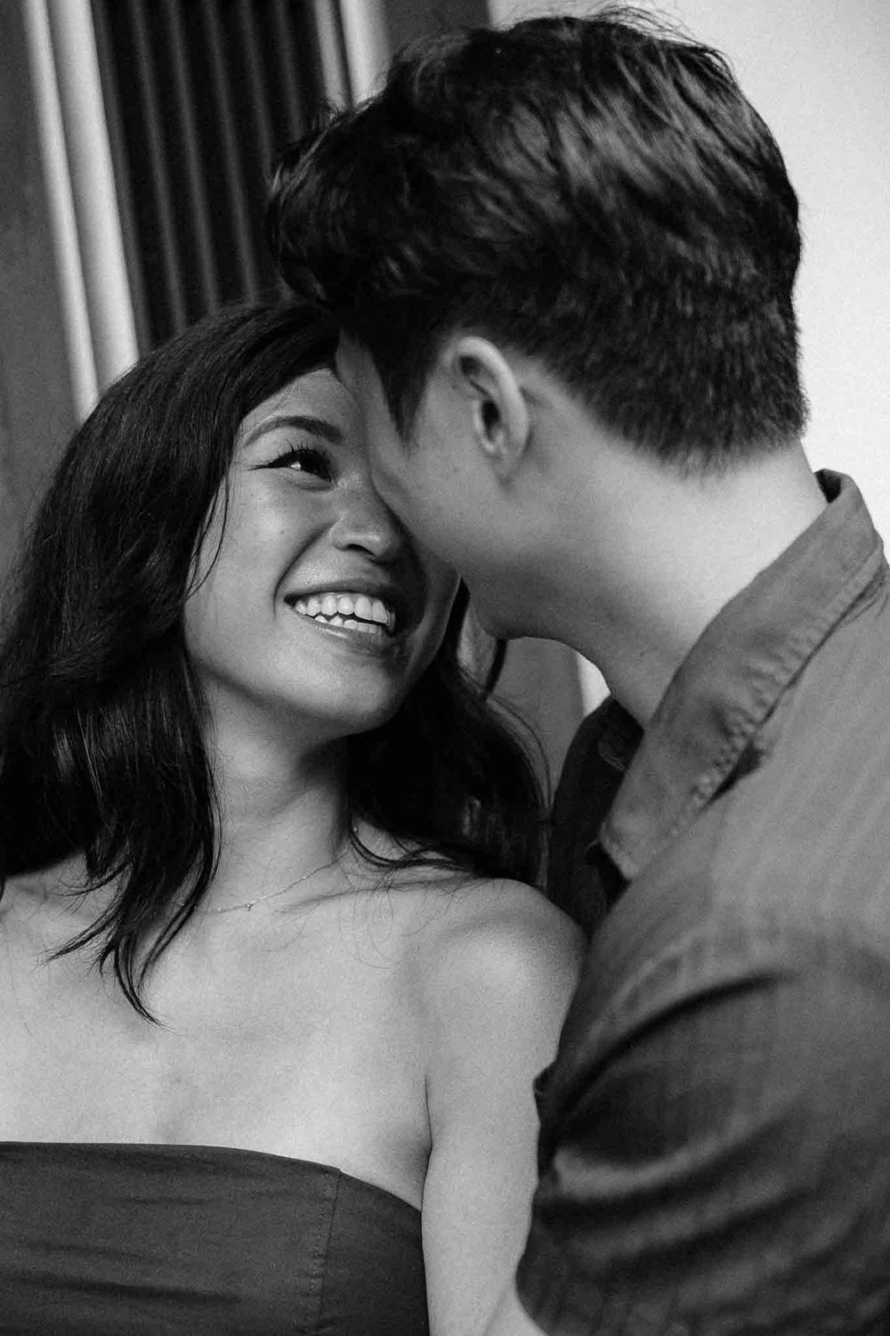 Black and white photo of a smiling young woman and man sharing a romantic moment together.