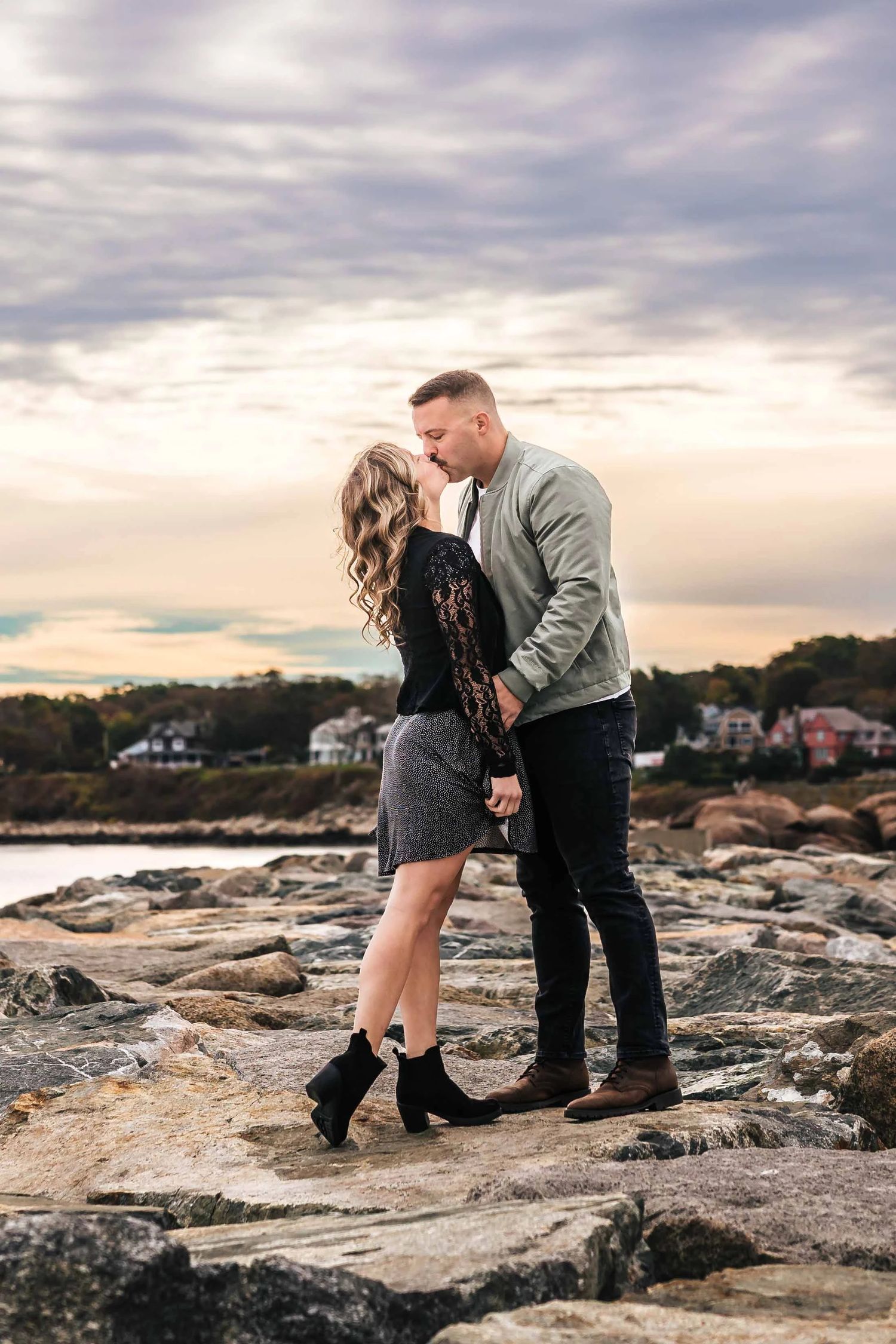 Couple embracing and about to kiss on granite breaker at dawn. Engagement at Rockport Harbor, Rockport, MA