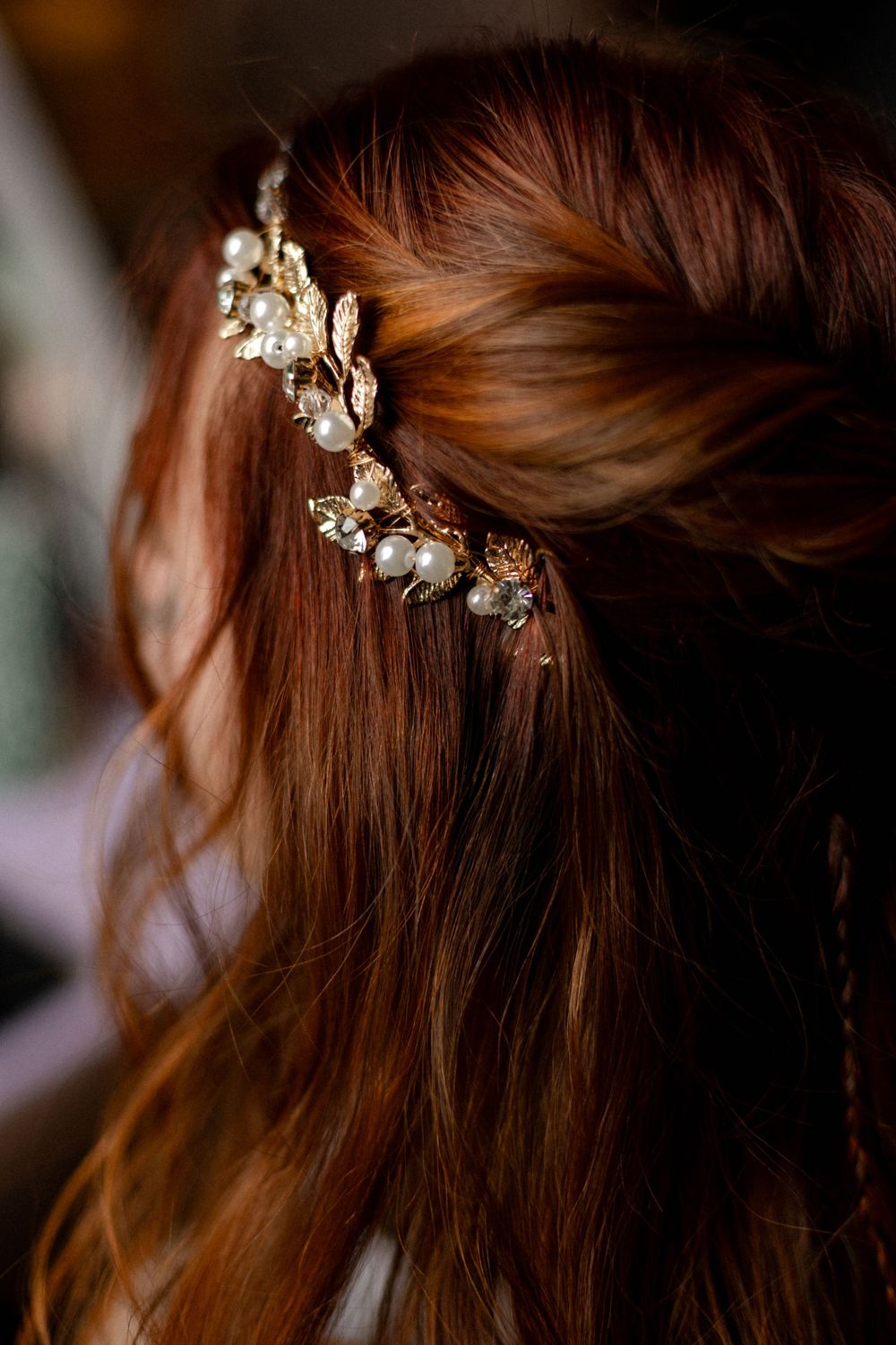 Close-up of a bride's long auburn hair adorned with a gold leaf hairpiece decorated with pearls.