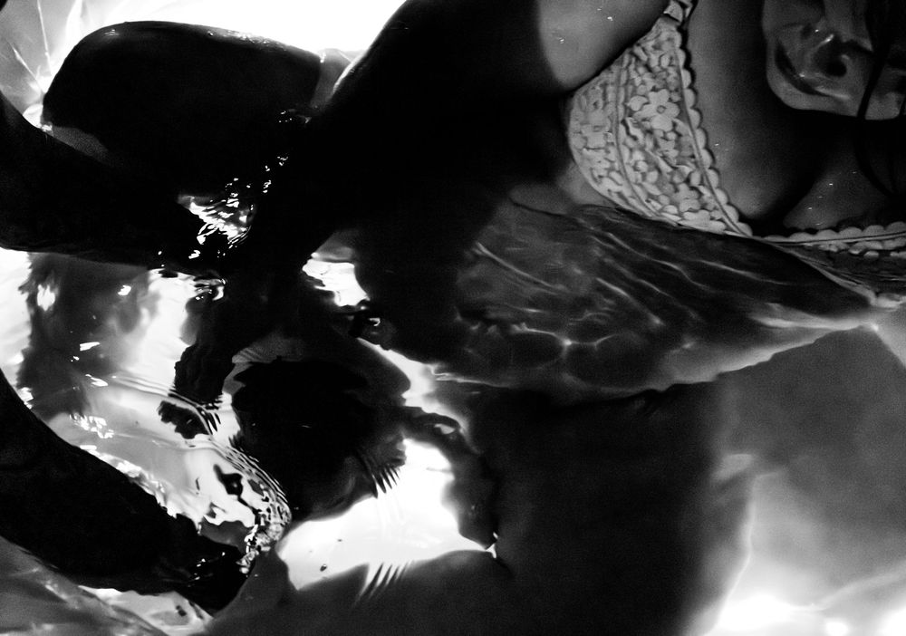 Black and white underwater photo of a person in lace swimwear with reflective water surface.