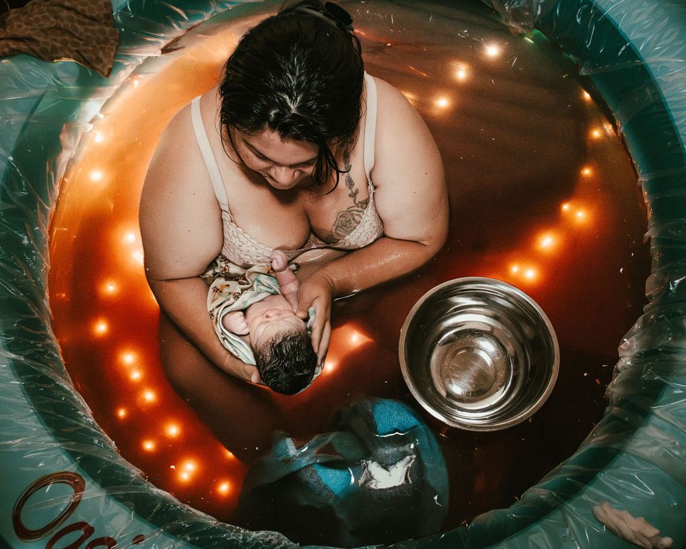 Aerial view of mother holding newborn in illuminated birth pool after water birth.