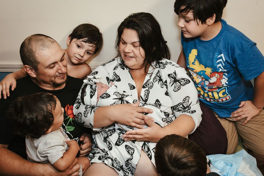 Family gathered around mother holding newborn baby on bed after home birth.