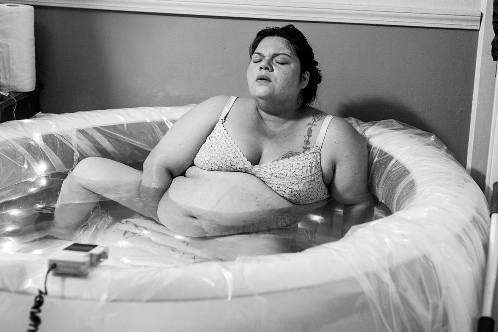 Black and white photo of a pregnant woman relaxing in an inflatable birthing pool during labor.