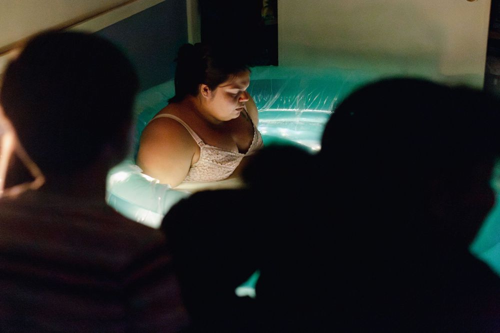 Woman illuminated by blue light viewed from behind silhouetted observers in a dark room.