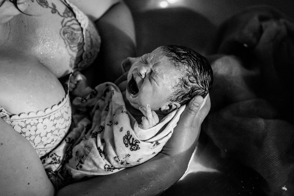 Black and white photo of a newborn baby being held by mother immediately after water birth.