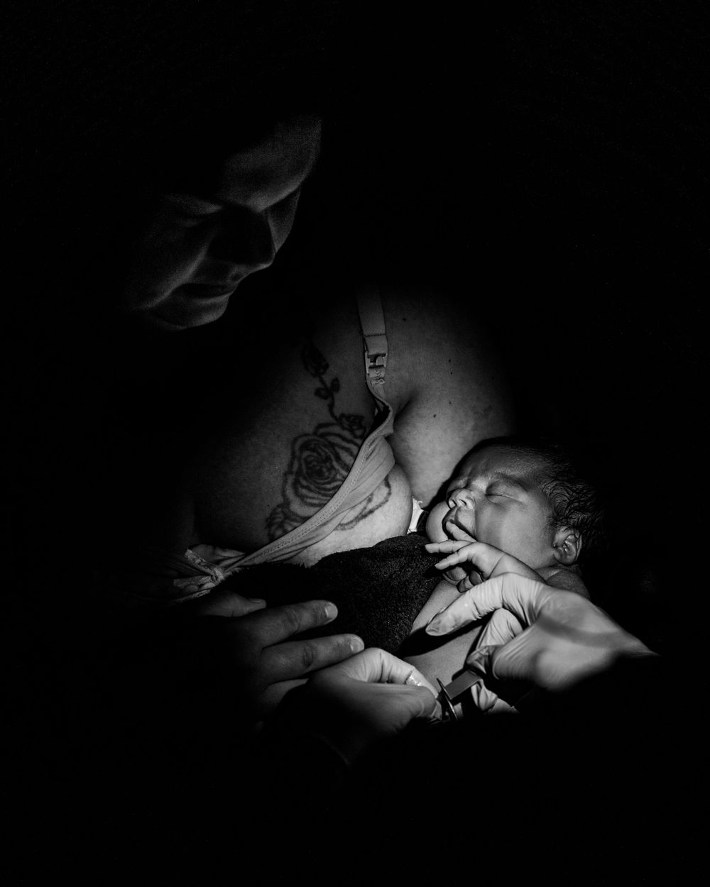 Black and white photo of a mother cradling her newborn baby, with a rose tattoo visible on her arm.