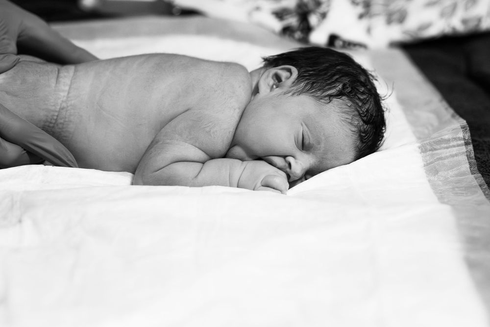 Black and white photo of a sleeping newborn baby lying on a white blanket.
