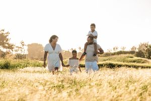 Family walking through golden sunlit field together, parents holding children's hands outdoors.