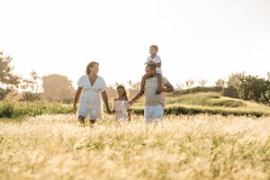 Happy family walking through a sunny golden field, parents holding hands with children on a warm day.