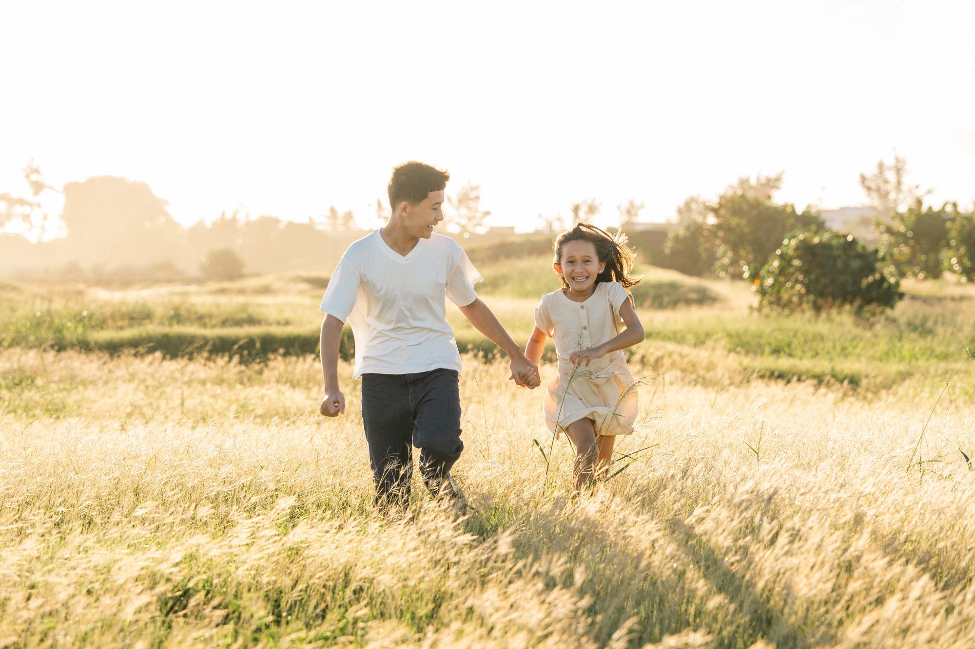 A joyful man and young girl run hand-in-hand through a sunlit golden field, smiling together.