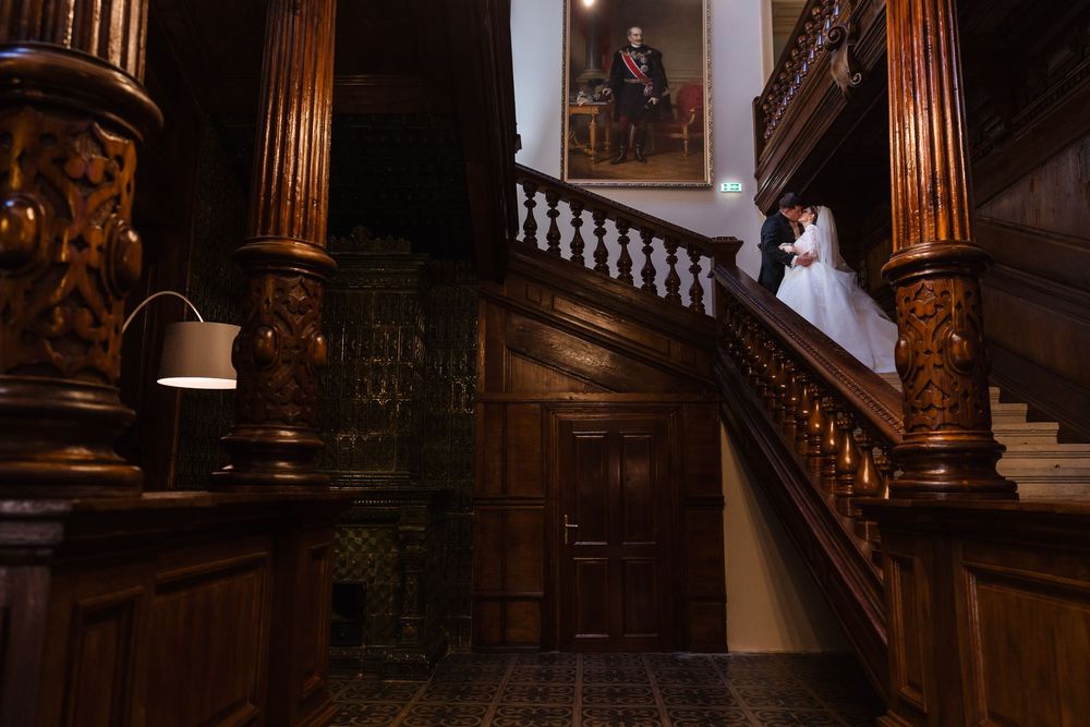 Bride and groom share a romantic moment on an ornate wooden staircase in an elegant historic venue.
