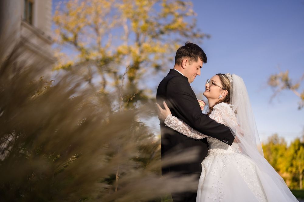 A bride and groom share a romantic embrace outdoors, with golden trees and soft sunlight in the background.