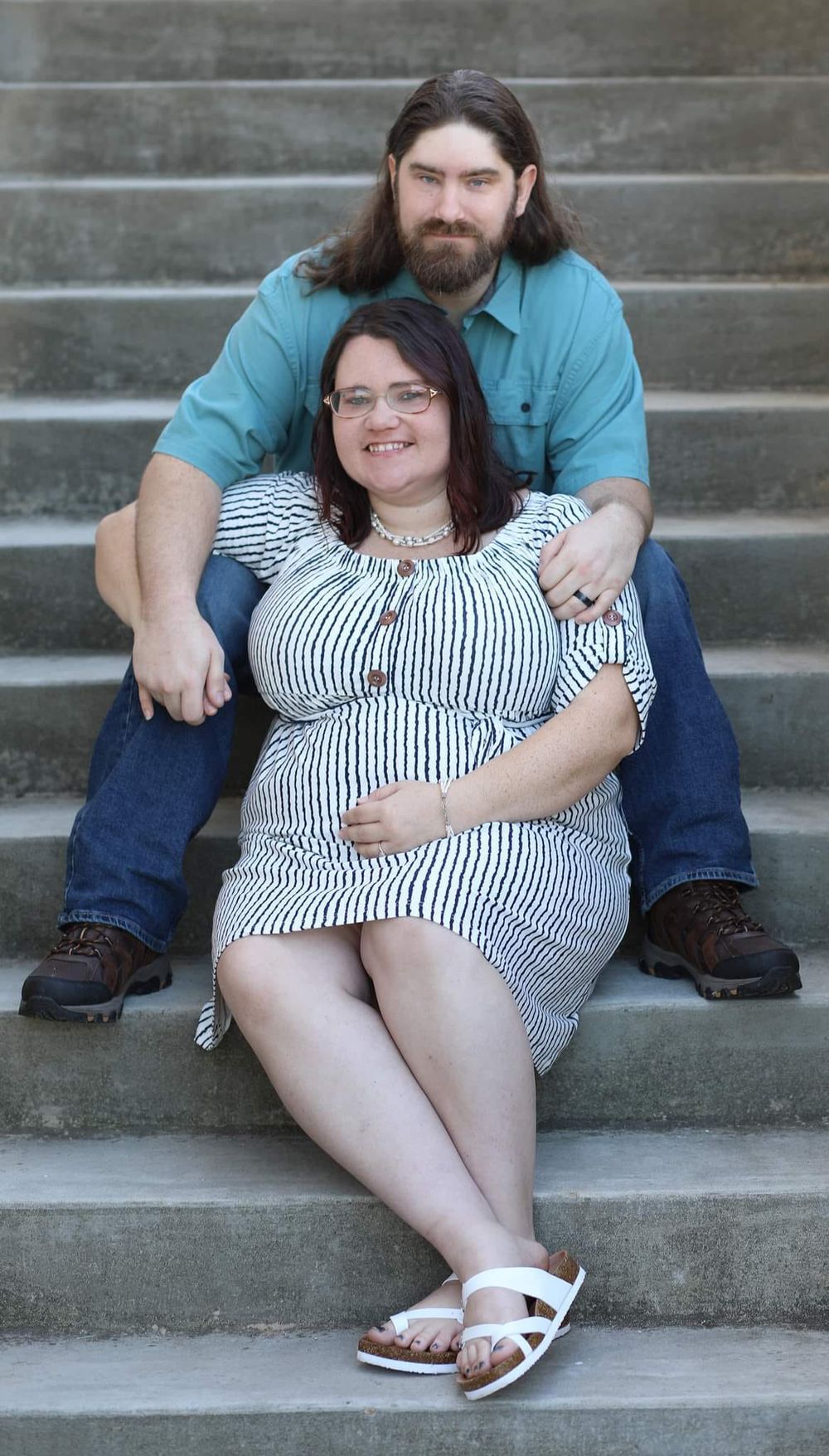 Smiling couple sitting on stone steps, woman in striped dress, man in teal shirt.