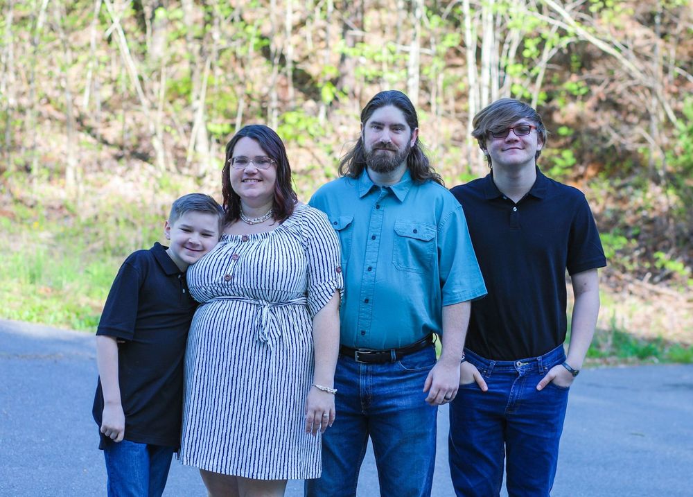 Family of four smiling together on a tree-lined path in spring outdoor setting.