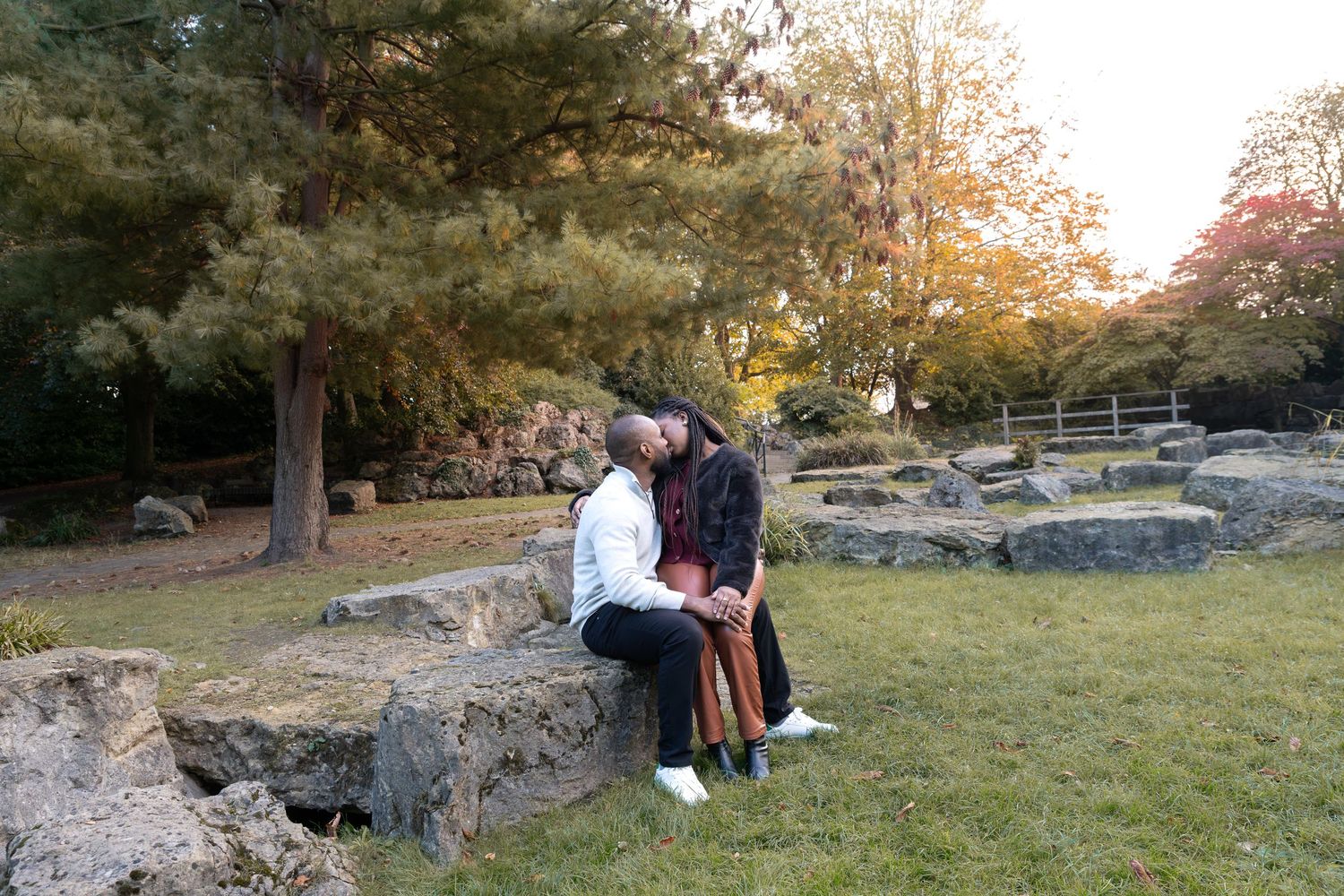 Couple sitting closely together on rocks in a serene autumn park with colorful trees and natural stone landscape. wedding proposal Rotherham