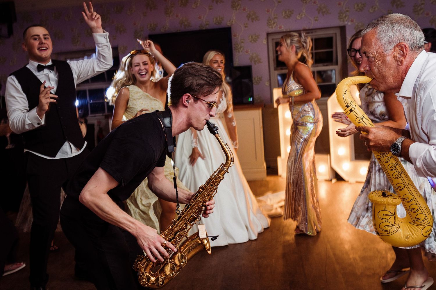 Saxophonist performs energetically at a lively wedding reception while guests dance and celebrate in formal attire.