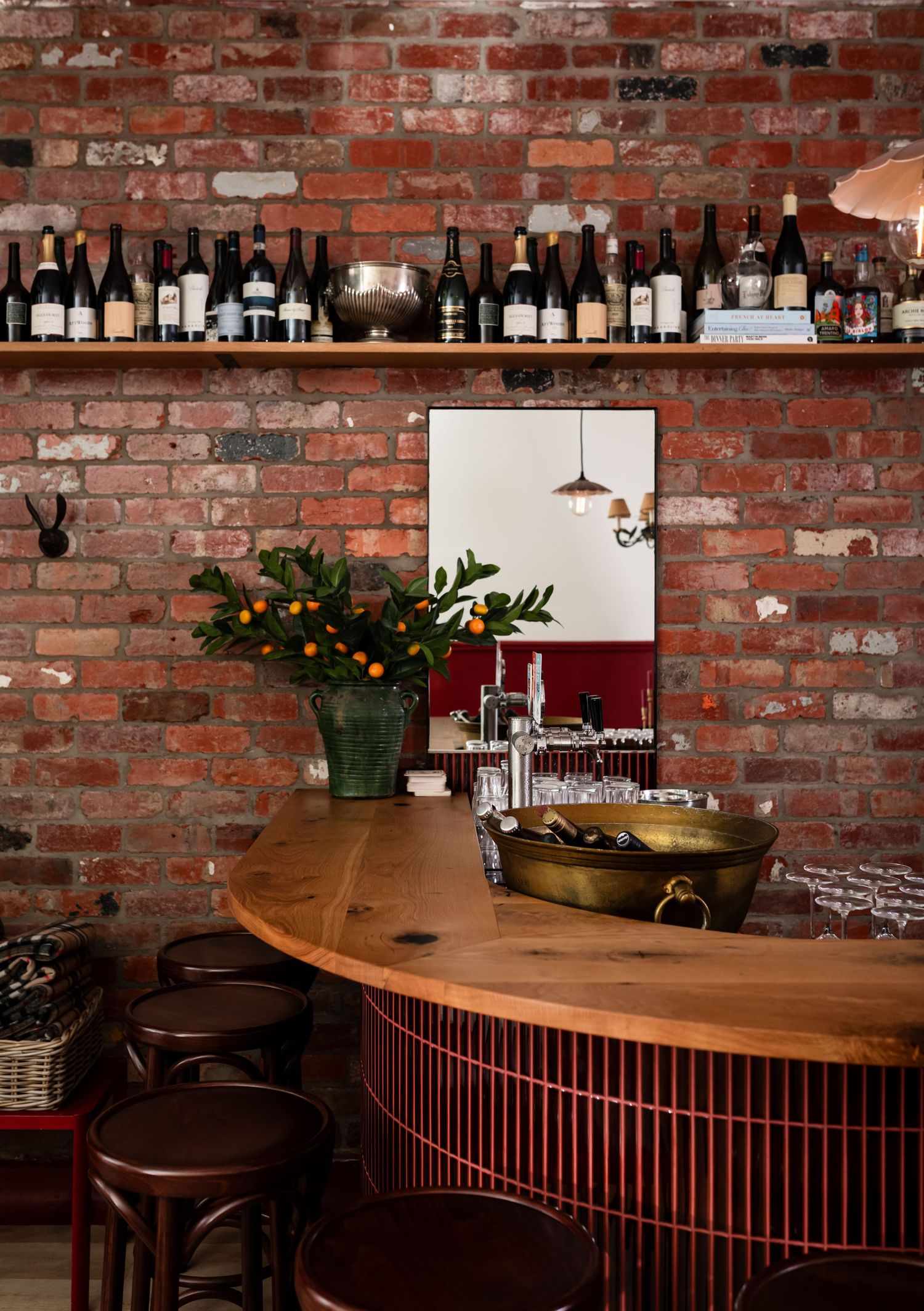 Rustic bar with exposed brick walls, curved timber counter, wine bottle shelf, brass ice bucket, leafy centerpiece and leather bar stools.