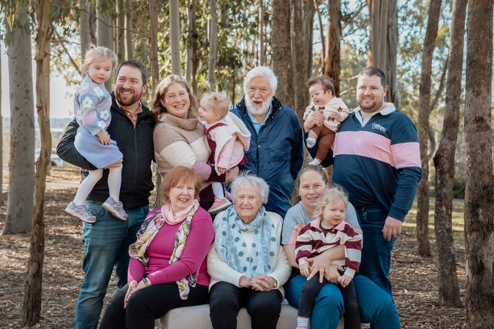 Multigenerational family of adults, grandparents and young children posing together among tall trees in a sunlit forest in Rouse Hill.