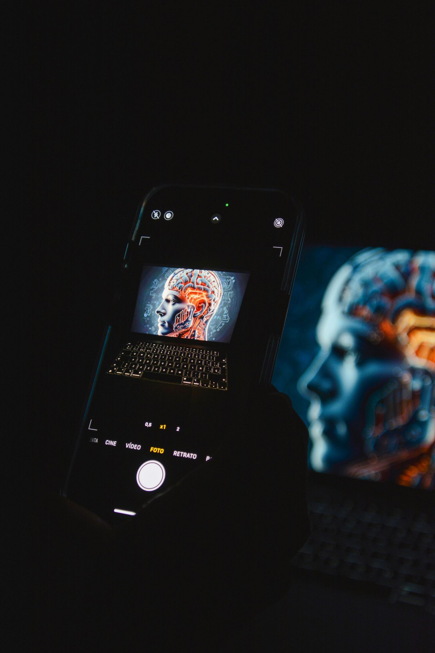 Smartphone photographing an AI human brain anatomy display on a laptop screen in a dark room with glowing robotic head artwork.