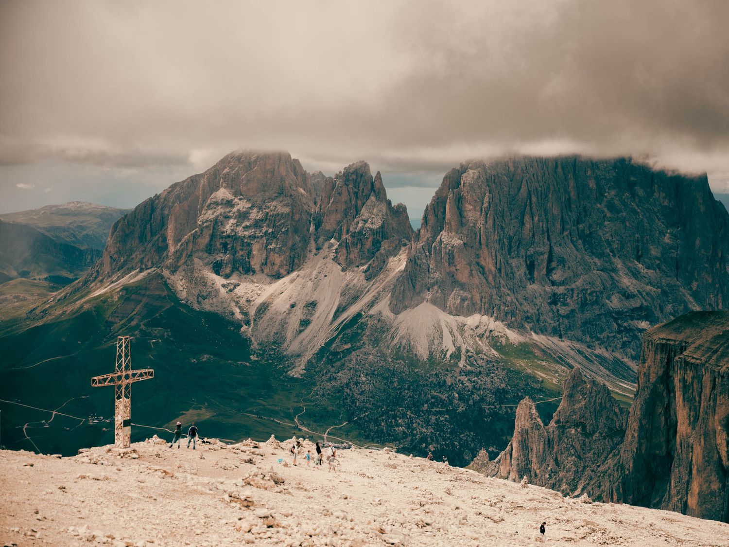 Dramatic Dolomite mountains with jagged rocky peaks, winding road, and moody overcast sky in the Italian Alps.